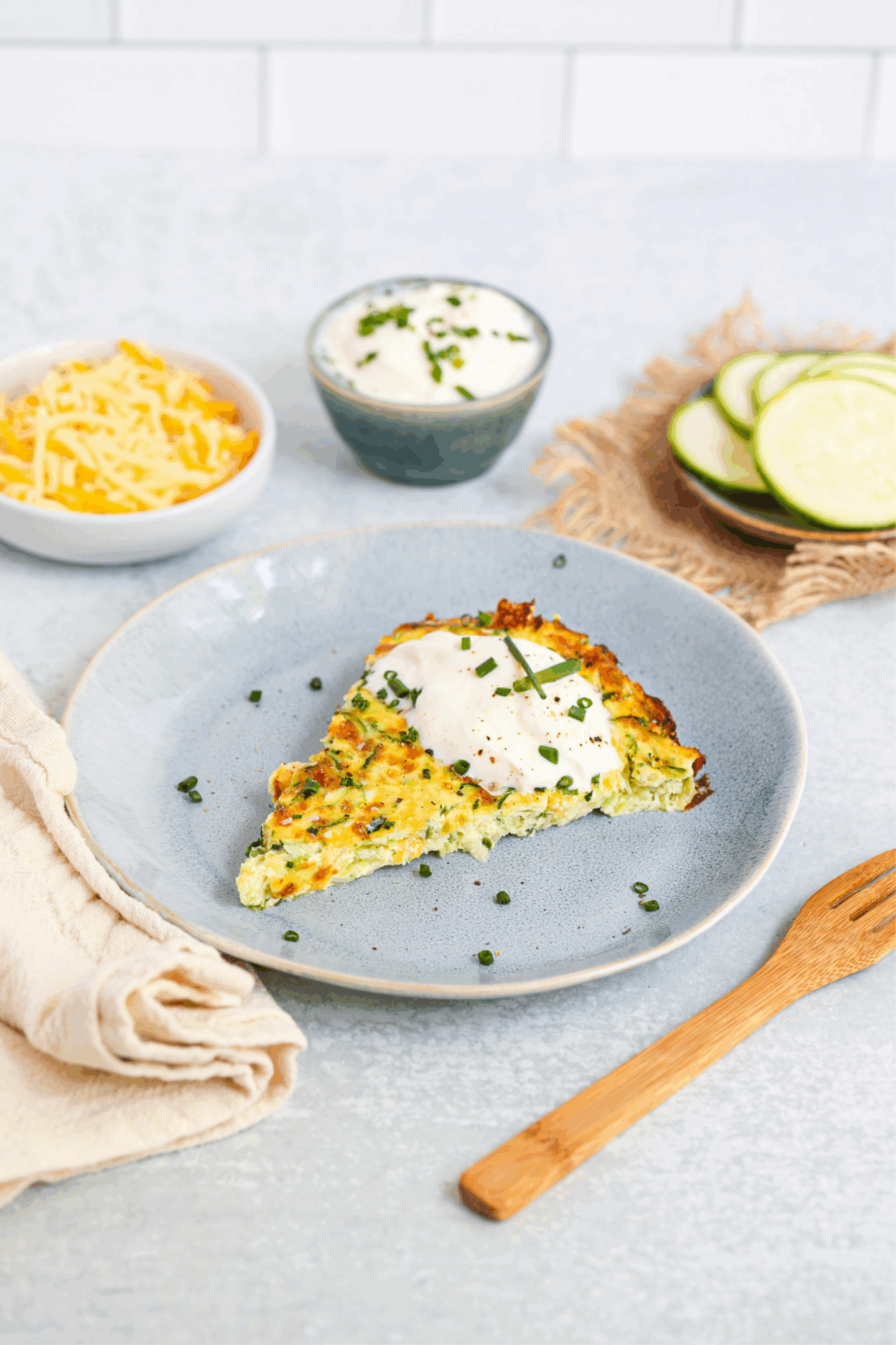 Finished Frittata on a table with a white background. Bowls of cheese, greek yogurt and zucchini surrounding.