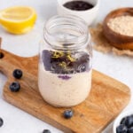 overnight oats with blueberry chia jam on a cutting board in a mason jar, surrounded by elements of the ingredients.