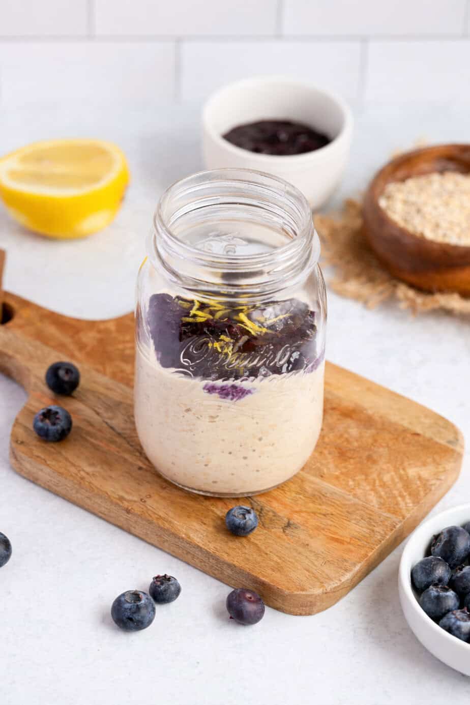 overnight oats with blueberry chia jam on a cutting board in a mason jar, surrounded by elements of the ingredients.