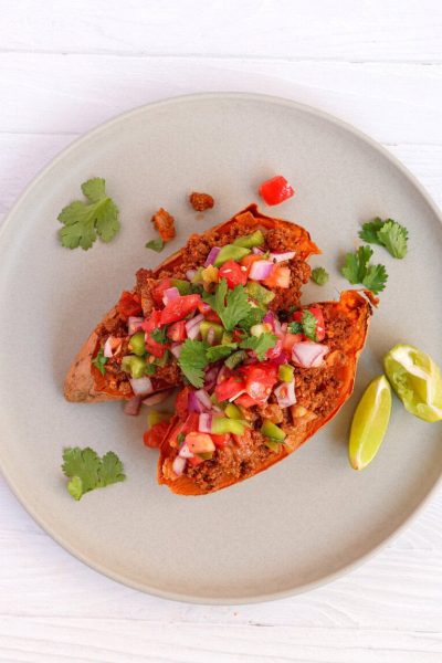 Overhead view of sweet potato taco boats topped with ground beef and fresh salsa, garnished with cilantro and lime wedges on a gray plate"