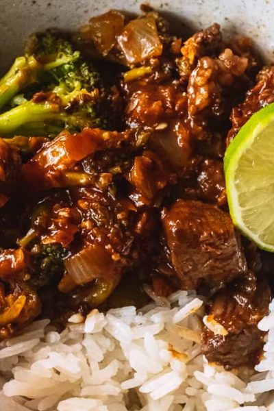 Beef and broccoli in a bowl with a lime and rice